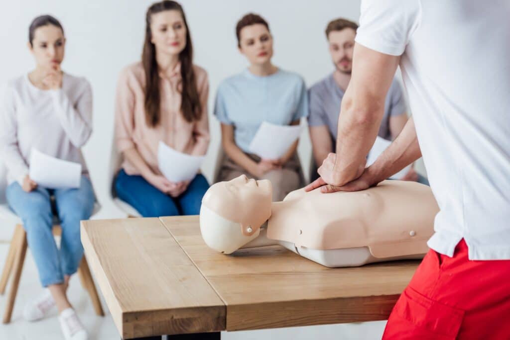 back view of instructor performing cpr on dummy during first aid training with group of people